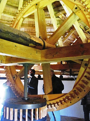 Dva pohledy na repliky vnitřního vybavení větrného mlýna: hlavní osa s převodem palečným a cévovým kolem a pohled na palečné kolo a vnitřní konstrukci střechy mlýna