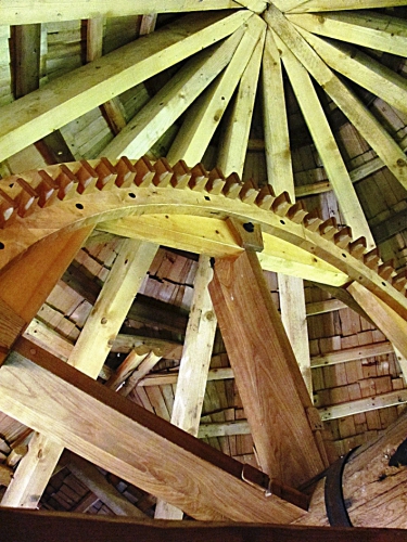 Dva pohledy na repliky vnitřního vybavení větrného mlýna: hlavní osa s převodem palečným a cévovým kolem a pohled na palečné kolo a vnitřní konstrukci střechy mlýna
