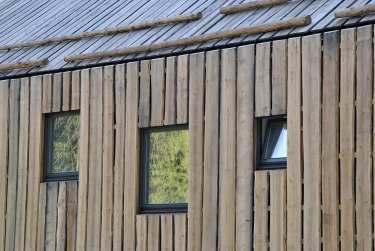 Fasády obou domů tvoří vertikální dřevěný obklad přecházející ze stěn na střechu