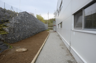 Obr. 4: Opěrná gabionová stěna, za zdí vlevo frekventovaná silnice, vpravo výrobní hala, před zdí zelený pás