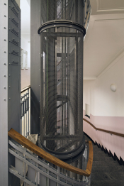 Šachta výtahu tvoří tubus z drátěné sítě, který svým zaoblením reflektuje tvar schodiště