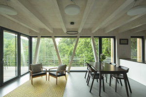 V interiérech je přiznaná konstrukce CLT panelů, prostor obývacího pokoje ozvláštňují šikmé pilíře a okno přetažené přes roh