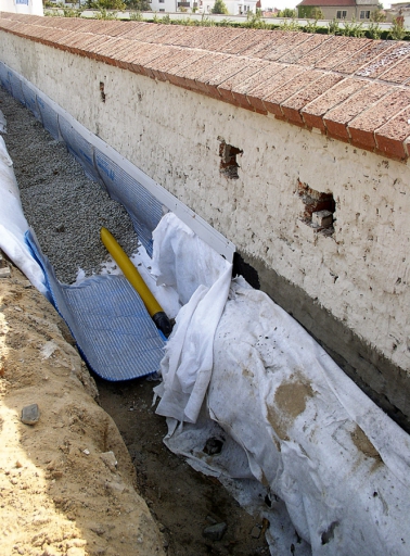Obr. 4: Zámek Troja – rozpracovaná drenáž při izolaci rozšířené části ohradní zdi pod chodníkem. Stěrkové izolace jsou chráněny profilovanou fólií, u terénu kotvenou pomocí lišty.